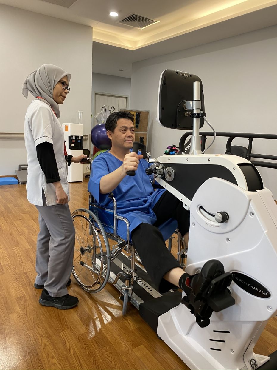 A stroke patient exercises his muscles with the help of a machine, supervised by a physiotherapist.